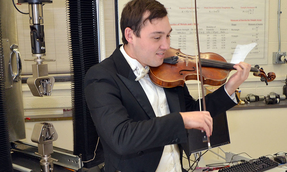 Feature image young man in a tuxedo plays the violin in a mechanical engineering lab