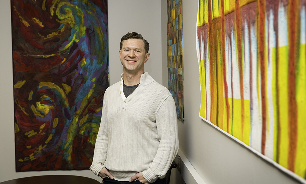 Feature image man standing in front of two pieces of art work
