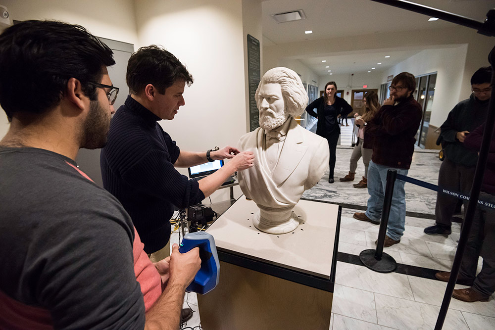 students and professor holding up a scanner next to the marble bust of Frederick Douglass