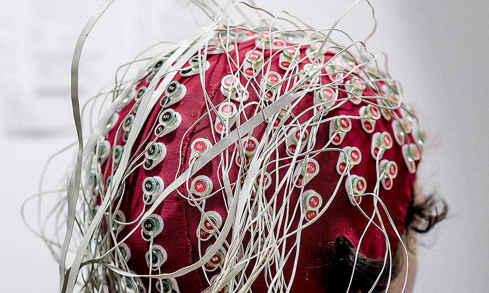 Feature image person sits with scalp cap and many wires capturing brain signals