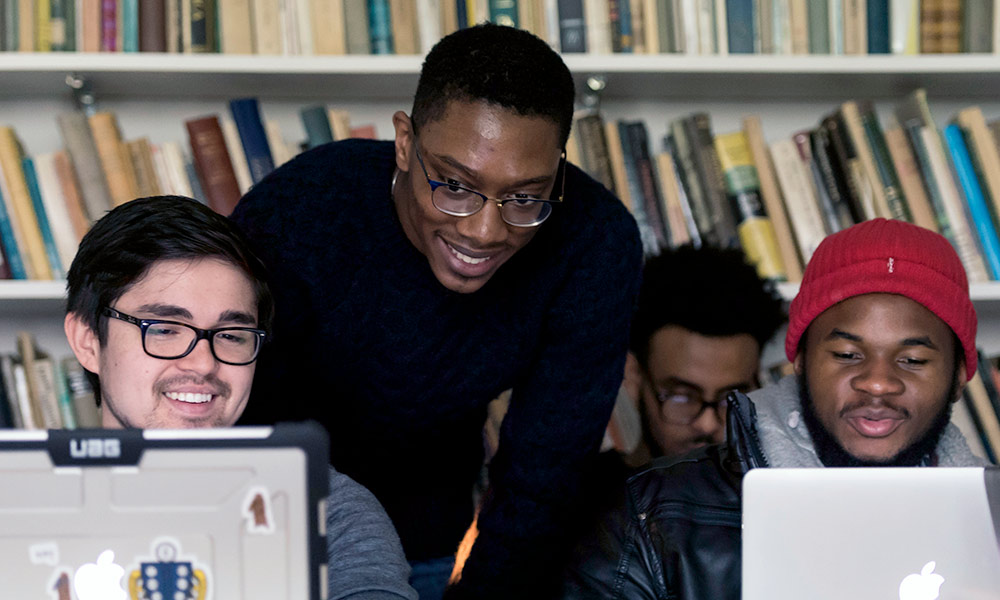 four students huddled around two laptops
