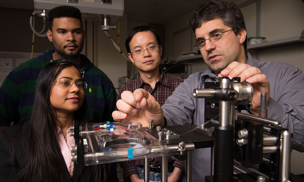 Feature image four people standing around optical instrumentation in a lab