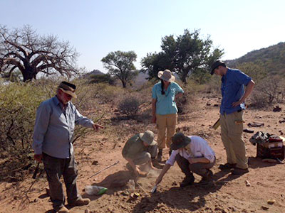group of researchers gather around a measuring device in a large, open field while studying the earth's magnetic field