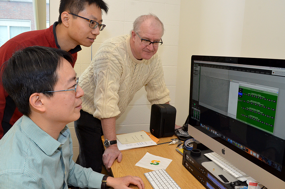 three researchers looking at a computer screen that shows sound levels