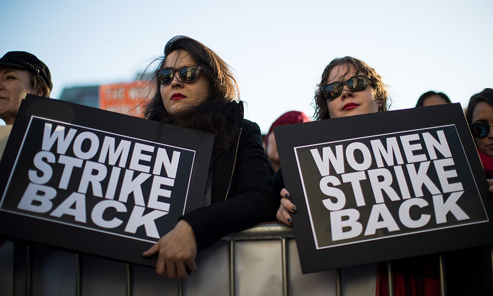 Feature image two women at a rally, each holding a sign that reads WOMEN STRIKE BACK
