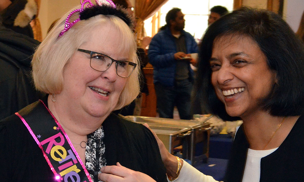 Feature image two women smiling for a photo, one wears a crown and a sash that reads RETIRED