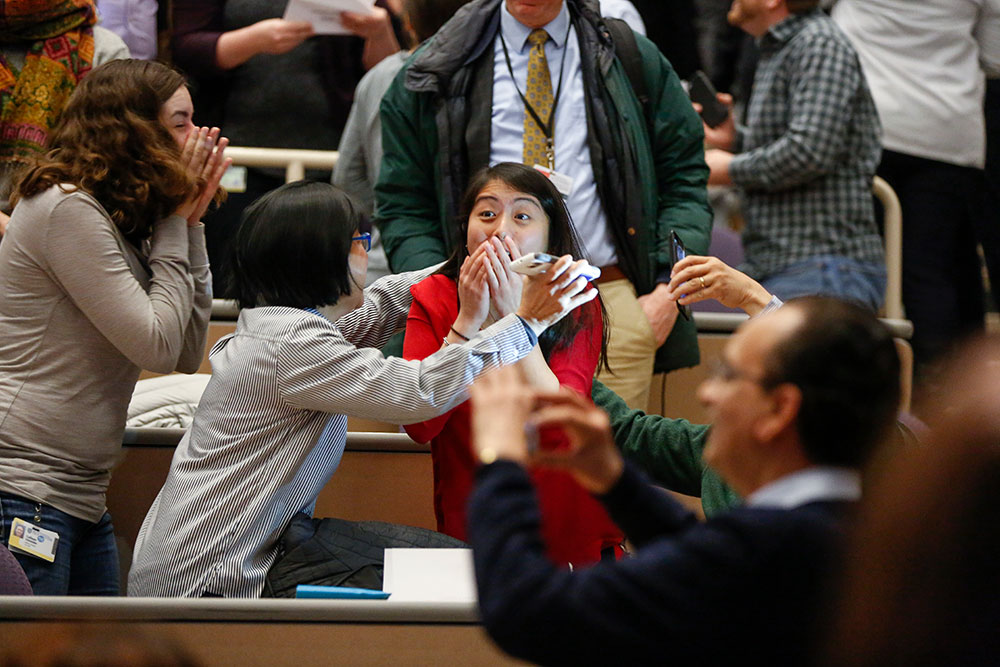 Feature image student with hands over her face in shock as family hugs here and cheers