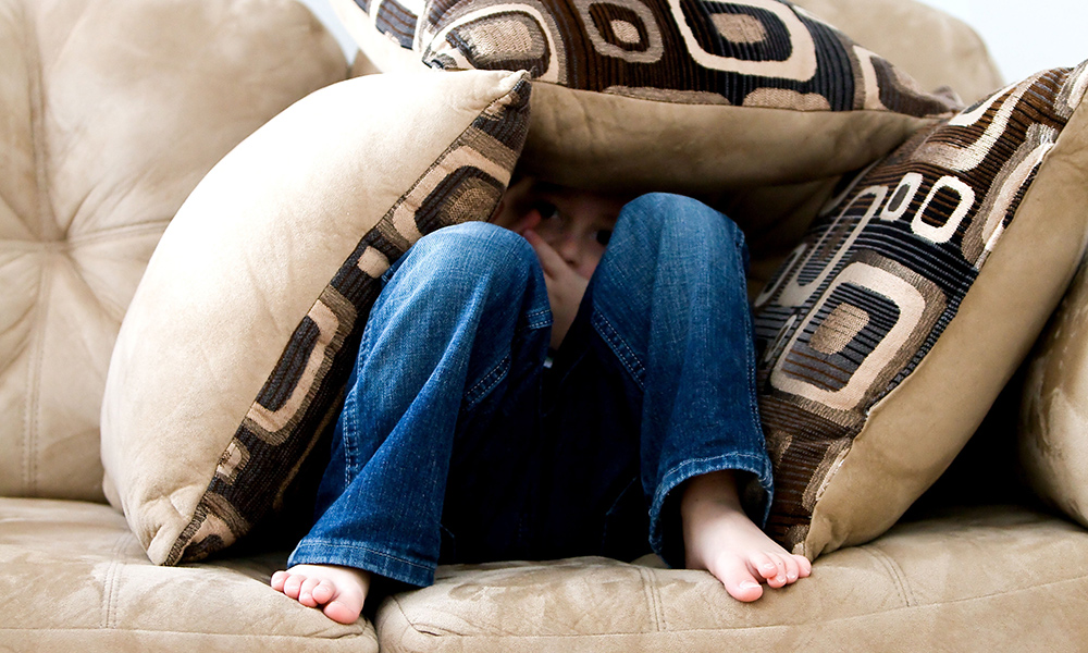 child hiding under sofa cusions
