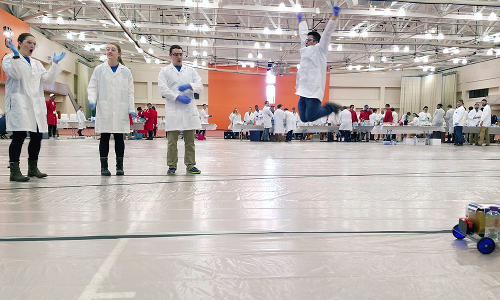 Feature image people jumping in lab coats at Chem-E-Car competition