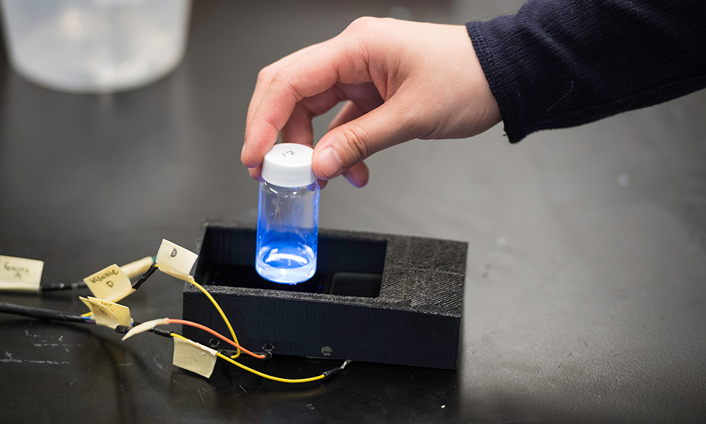 Feature image hand holds a glowing vial on top of a small black box