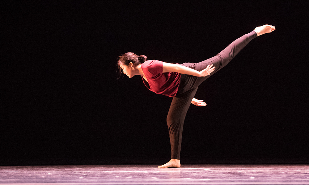 single dancer on stage raises leg behind her.