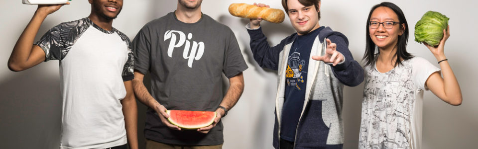portrait of four students, one holding a gallon of milk, one holding a watermelon, one holding a loaf of bread, one holding a head of lettuce