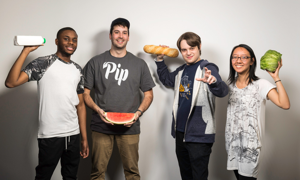 Feature image portrait of four students, one holding a gallon of milk, one holding a watermelon, one holding a loaf of bread, one holding a head of lettuce
