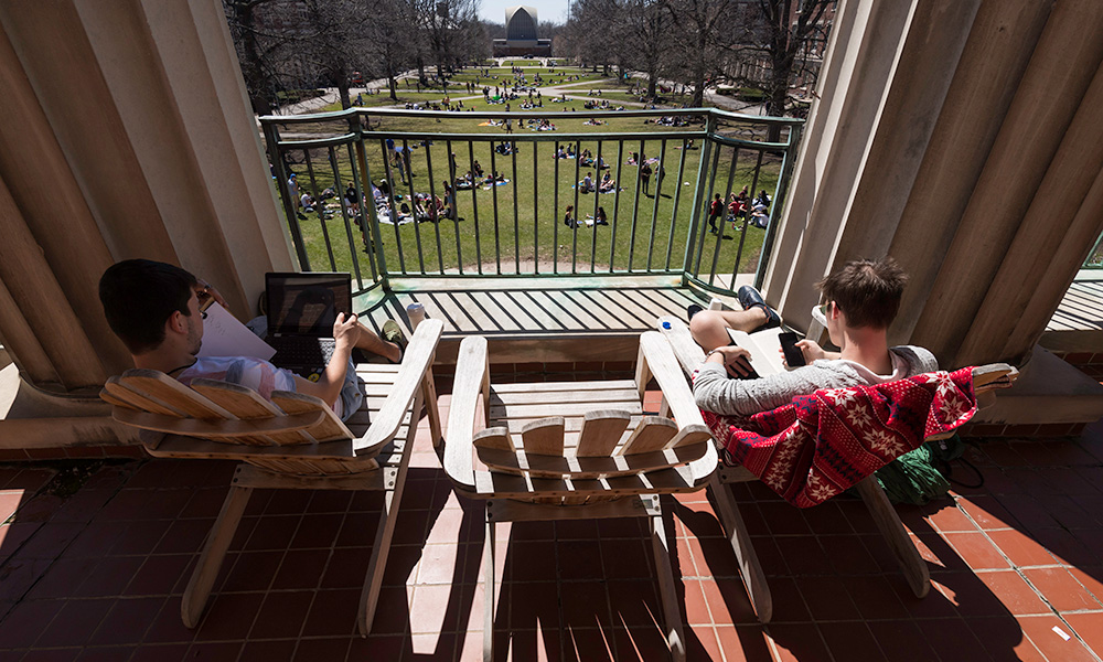 students sitting on Adirondack chairs on the library balcony on a sunny day