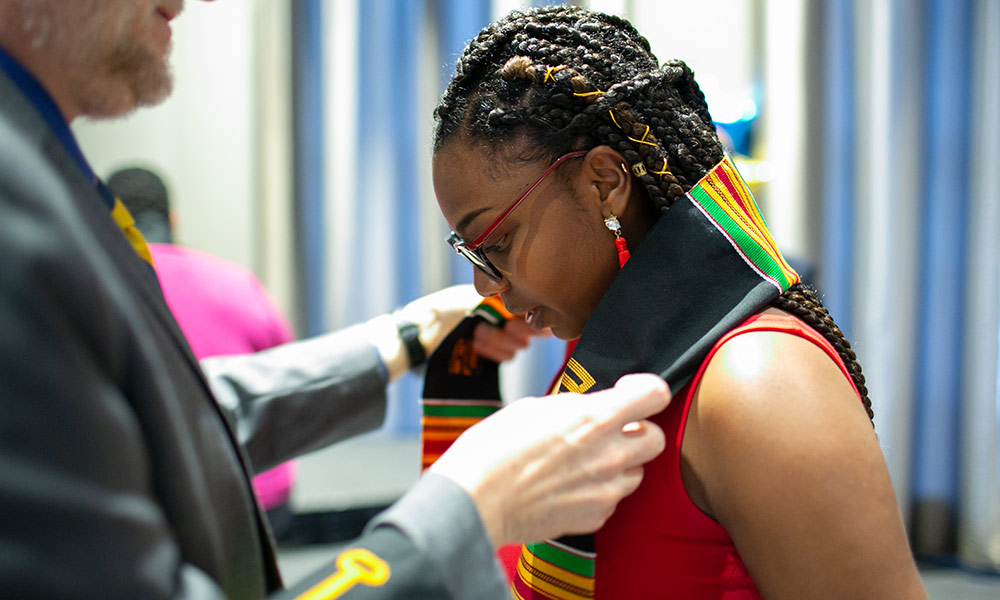 student receiving a brightly colored stoll over her shoulders
