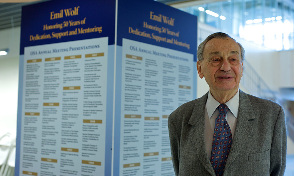 Emil Wolf standing in front of a sign marking hig 50th anniversary as a Rochester faculty member