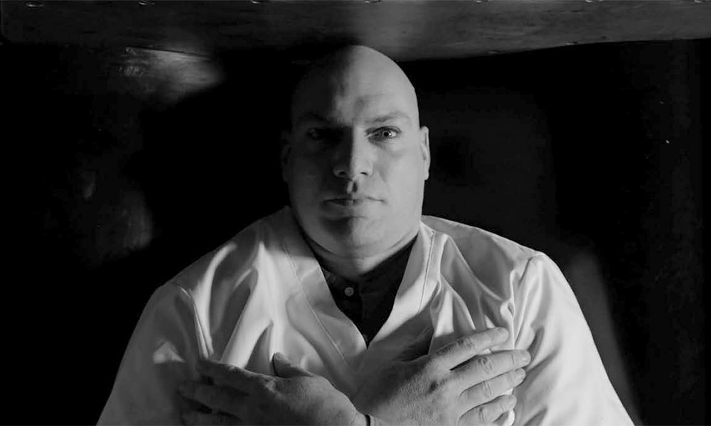 Feature image still from a black and white film shows a person lying in a box like a vampire