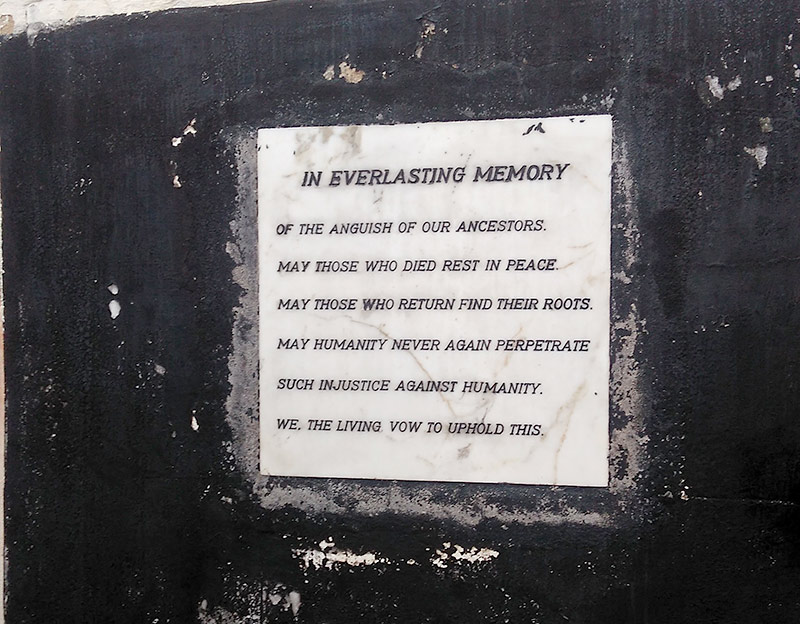 sign on a wall tha reads IN EVERLASTING MEMORY OF THE ANGUISH OF OUR ANCESTORS. MAY THOSE WHO DIED REST IN PEACE. MAY THOSE WHO RETURN RIND THEIR ROOTS. MAY HUMANITY NEVER AGAIN PERPETRATE SUCH INJUSTICE AGAINST HUMANITY. WE, THE LIVING, VOW TO UPHOLD THIS.