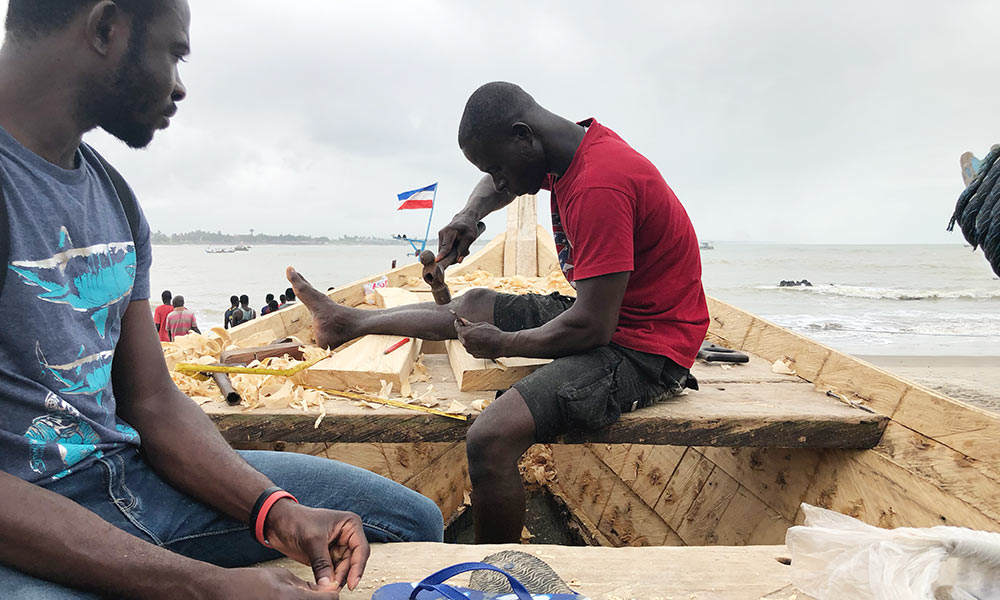 two men working on a wooden boat in Elmina, Ghana