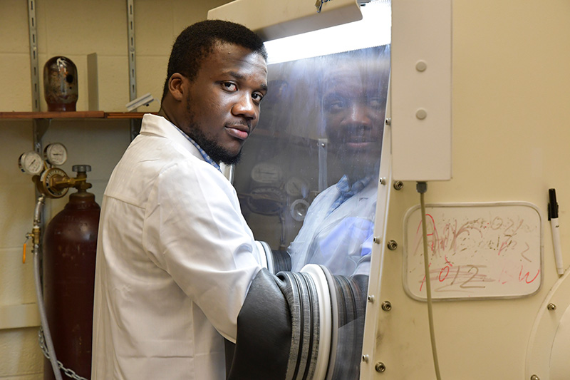 student in a lab coat with his hands working through a rubber sleeve