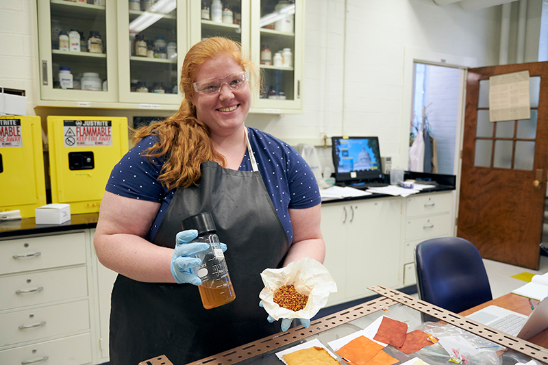 student in a lab apron holding a liquid dye and dye crystals