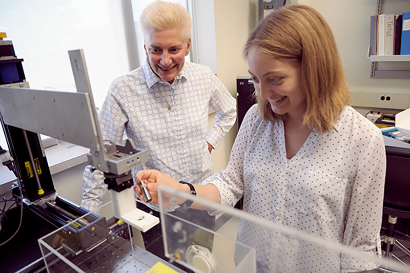 student and professor in the lab in front of a microscope