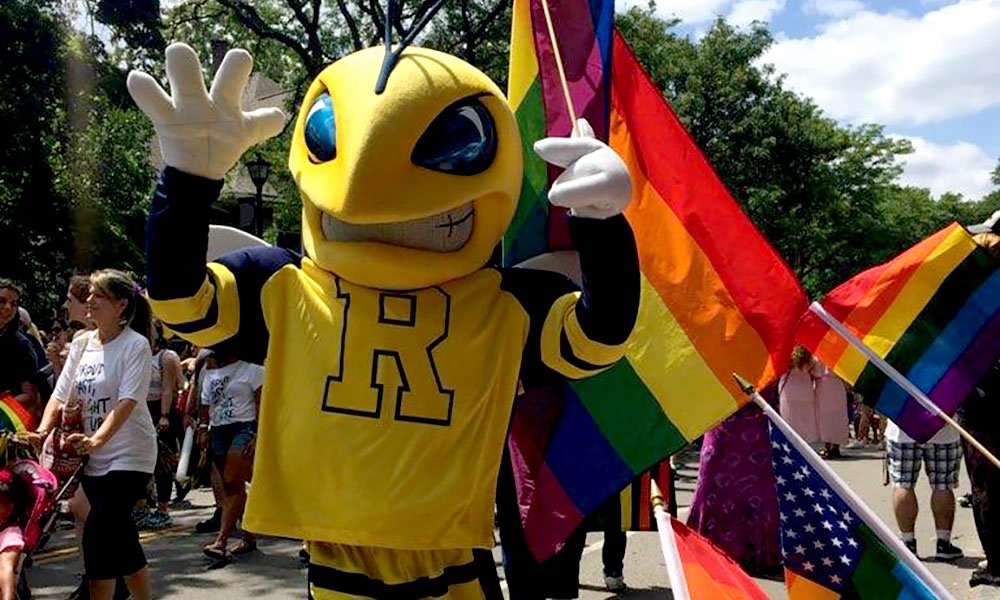 Rocky the Yellowjacket mascot marches in Pride Parade with a rainbow flag