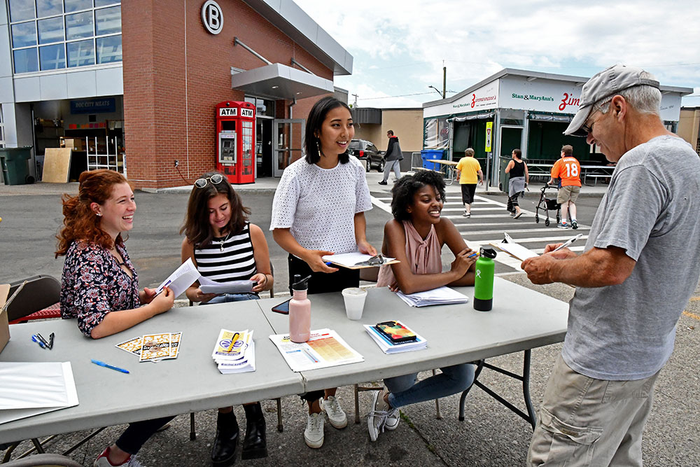 four students sitting behind a table at the public market as one customer fills out a survey