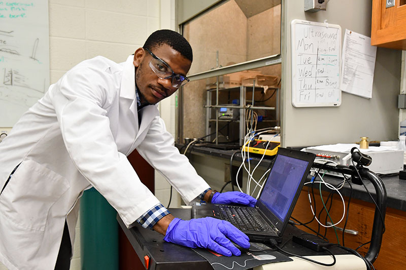 student in a lab coat, working with a laptop