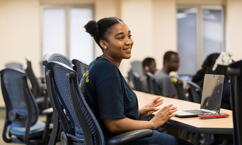 Feature image student smiling, sitting at a desk