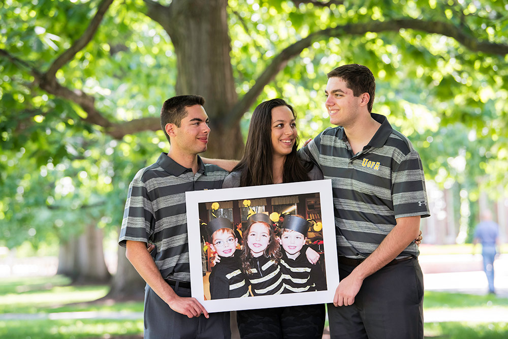 Feature image three students, holding another picture of themselves as children, dressed in bumblee costumes