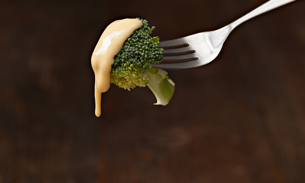 Feature image cheese sauce dripping off a piece of brocolli to illustrate lipid droplets