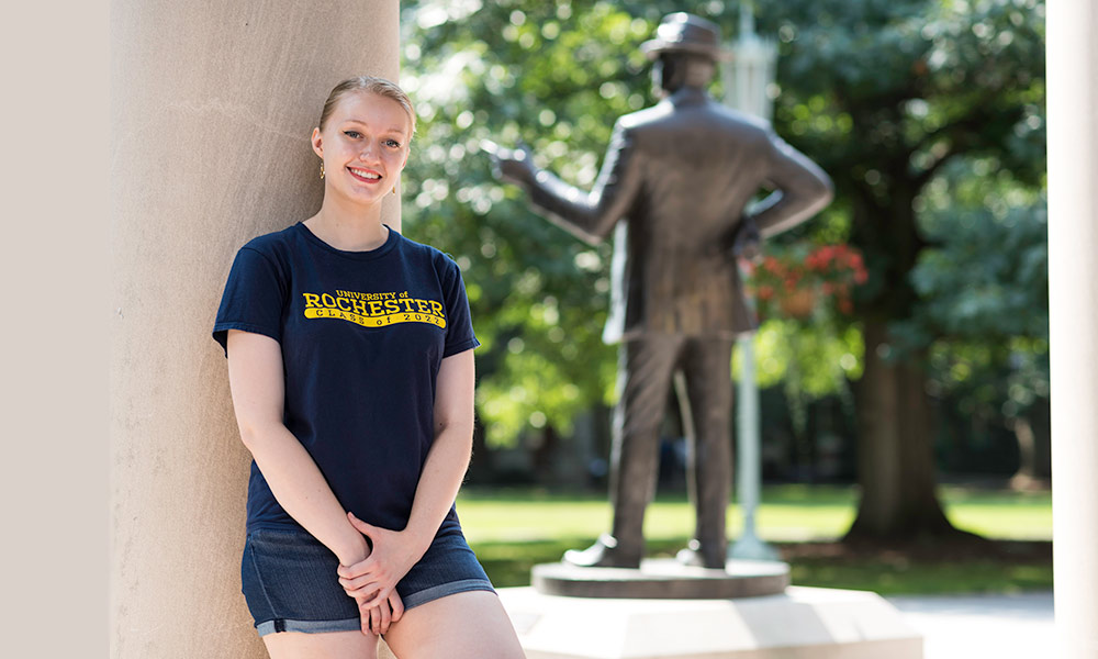 Feature image student leaning against a pillar, statue of George Eastman in the background