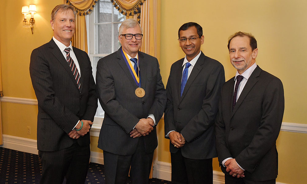 group photo of four people, one with a medallion around his neck