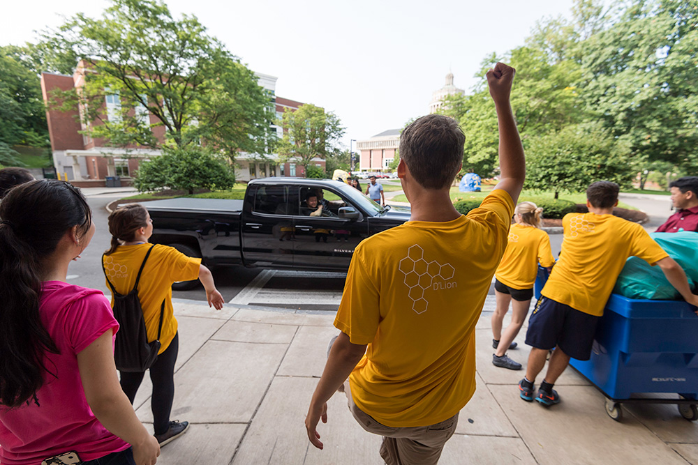 one student raises his arms in celebration and cars arrive in front of residence hall building