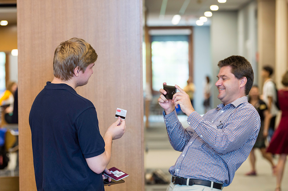 student holds up his ID card while father takes a picture