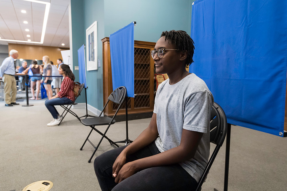 student sits in front of a large blue screen getting theri ID picture taken