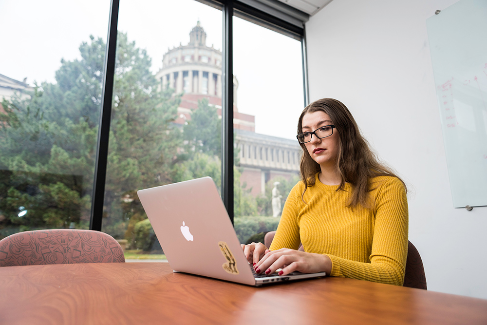 portrait of Wednesday Bushong at laptop with Rush Rhees Library in the background