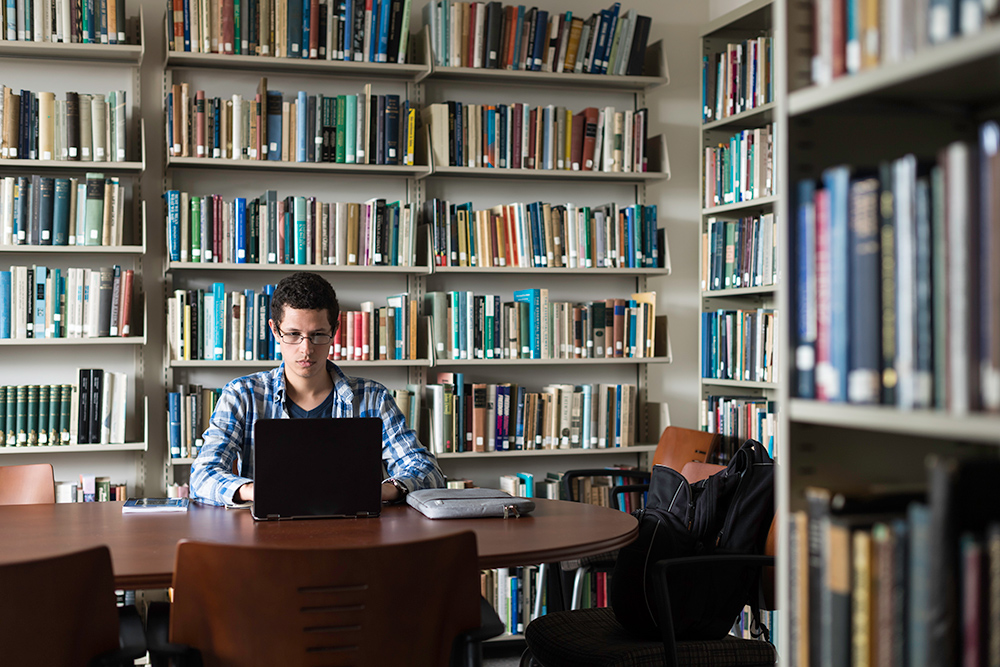 portrait of Yanssel Garcia in front a large bookcase filled with books