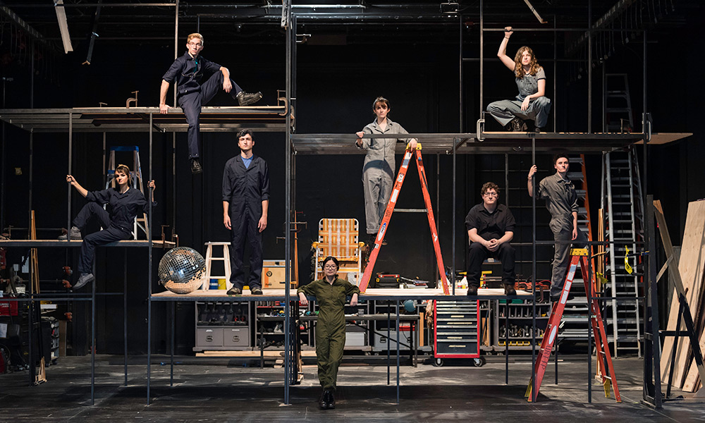 large groups of actors, standing on a tall scaffold on a stage