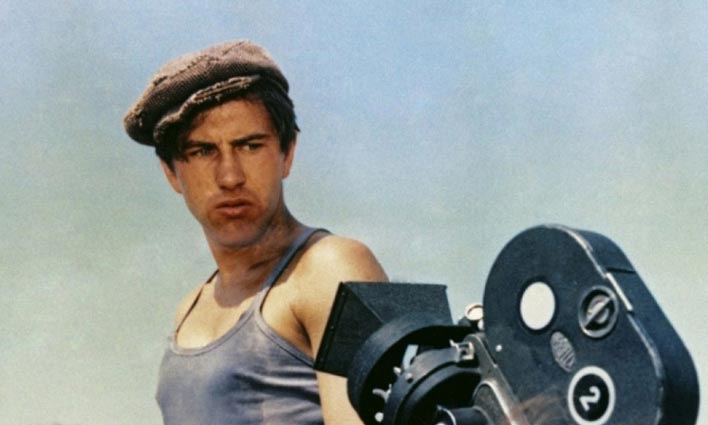 a man in a newsboy cap looking at a 1930s camera