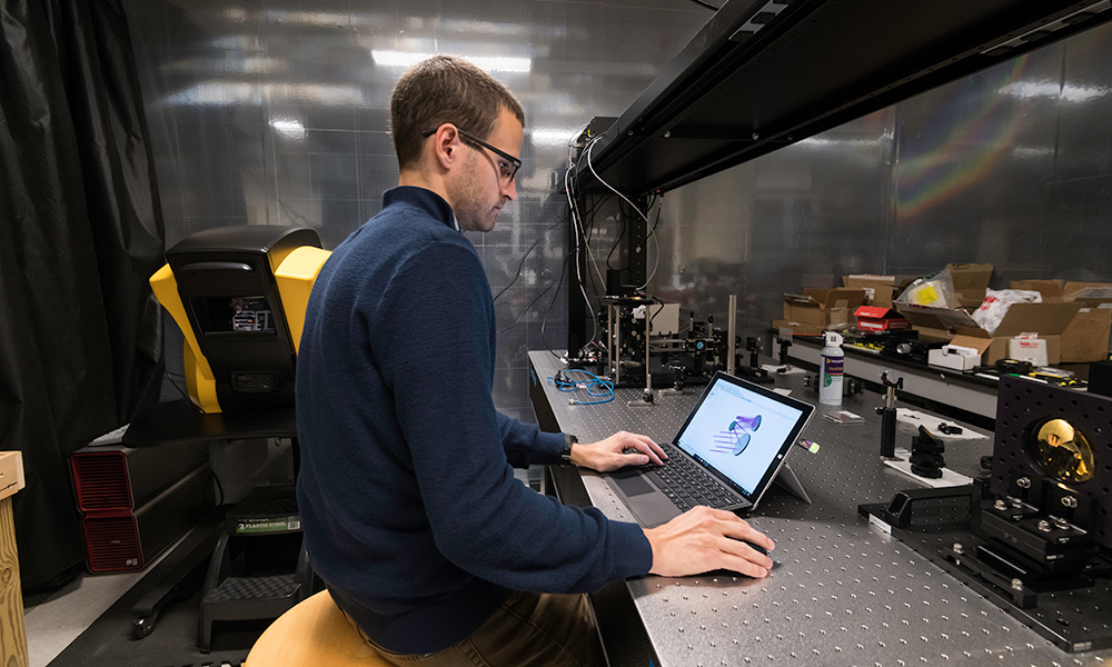 Aaron Bauer at a workbench looking at a design on his laptop