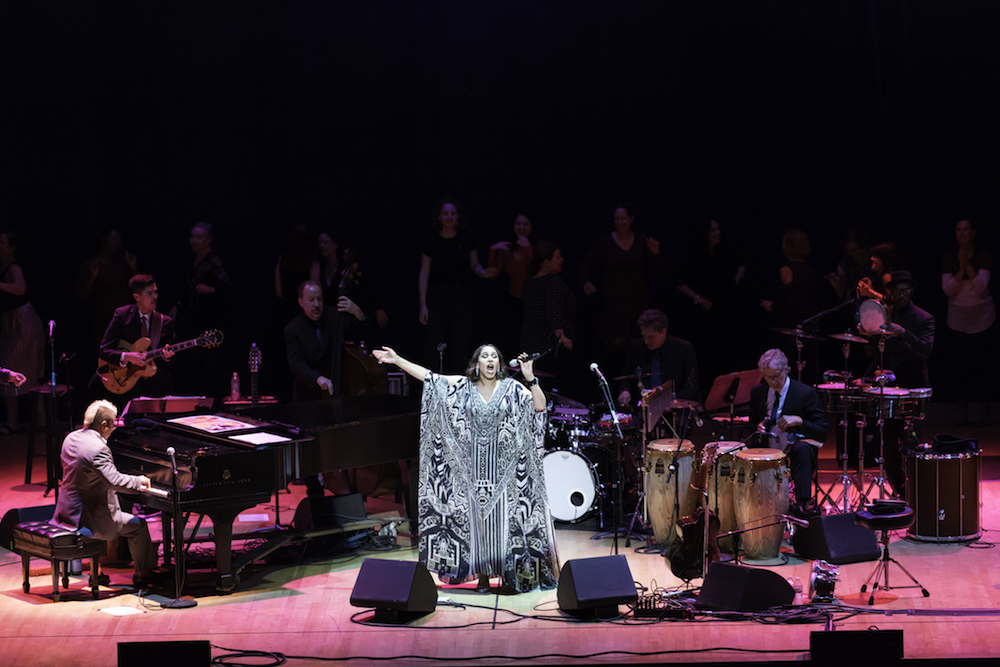 woman sings on stage surrounded by musicians