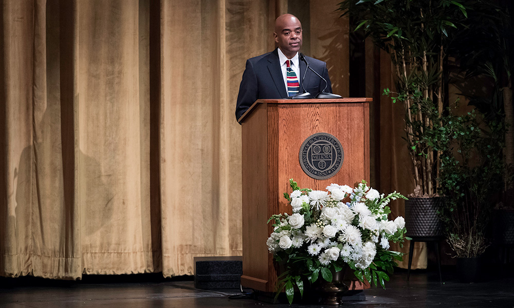 Feature image Lee Koonce speaking from a podium on stage at Strong Auditorium