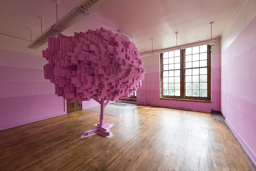 classroom painted in different shades of pink stripes with a large geometric sculpture in the center of a tree
