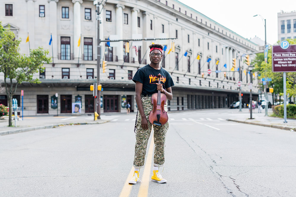 portrait of a student holding a viola and standing in front of the Eastman Theatre.