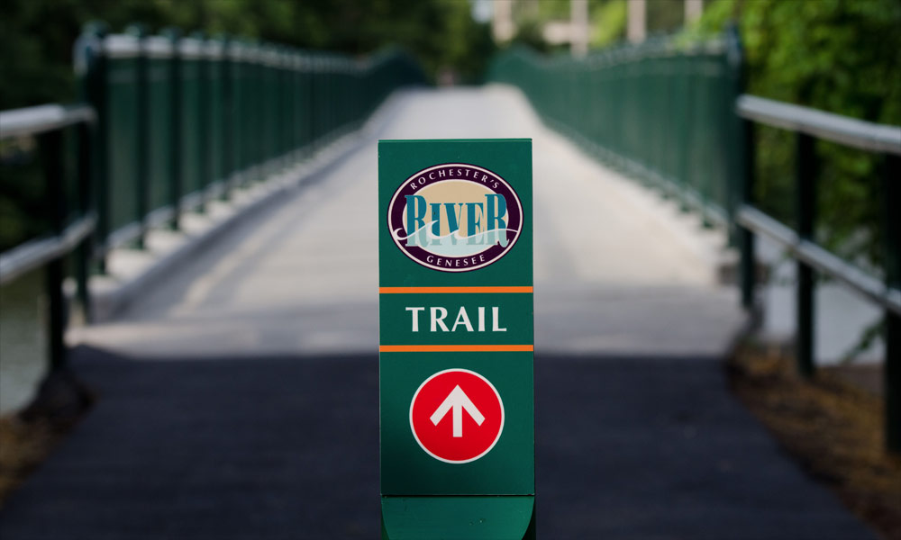 Feature image River bike trail sign leading over a bridge near the University of Rochester