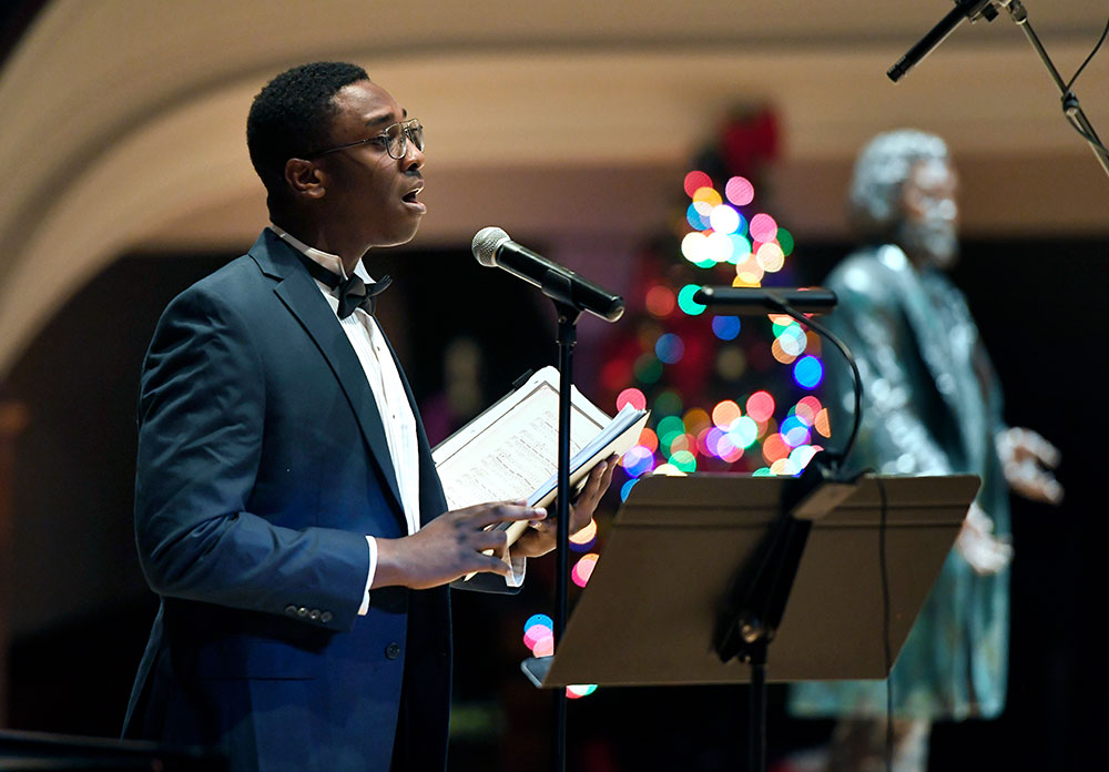Feature image singer on stage, with a sculpture of Frederick Douglass in the background