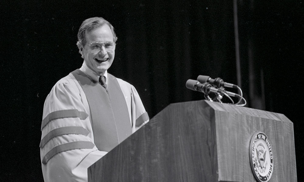 Feature image black and white photo of George H. W. Bush in academic attire standing behind a podium