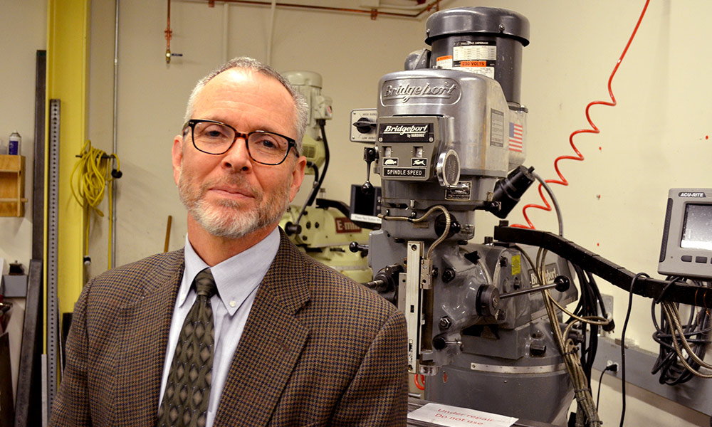 Jim Zavislan stands in front of a optics grinder in Rettner Hall.
